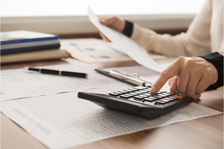 A woman is using a calculator on a desk.